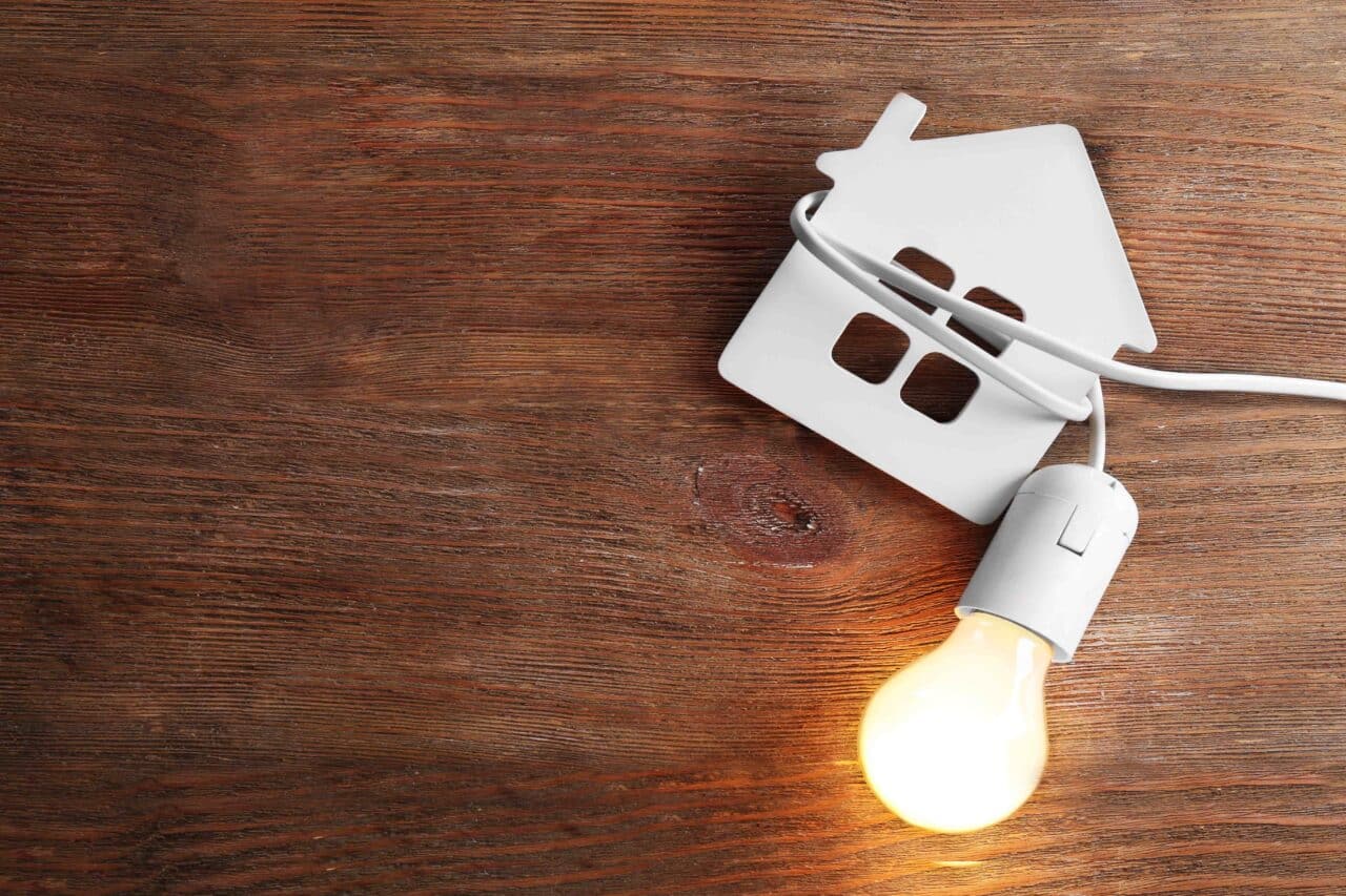 Bulb and shape of home on wooden background representing electrical warning signs in the home